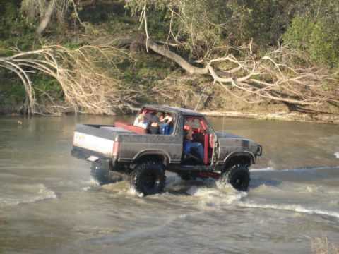 2001 Jeep Wrangler - Modified off-road truck with people in the cab driving through a river.