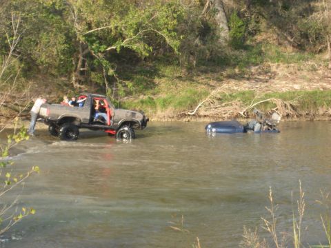 2001 Jeep Wrangler - A modified pickup truck with passengers navigates a river, while another car is submerged in the water.