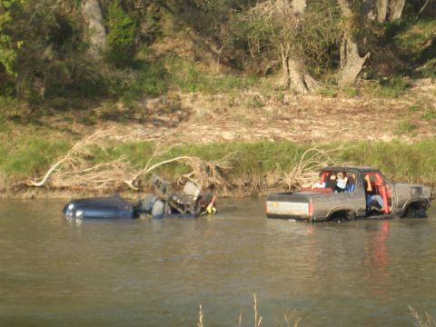 2001 Jeep Wrangler - A pickup truck and a sedan are stuck in a river, with people visible in the truck's cab.