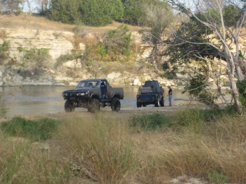 2001 Jeep Wrangler - Two trucks are parked near the water's edge on a dry riverbed, with one person observing the scene.