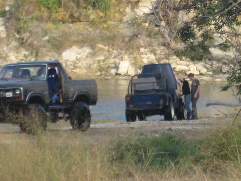 2001 Jeep Wrangler - Two off-road vehicles are parked near a river, with two people attending to one of them.