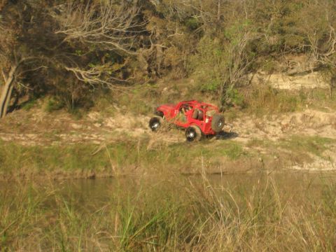 2001 Jeep Wrangler - A red Jeep Wrangler is parked on a dirt bank with trees and brush in the background.