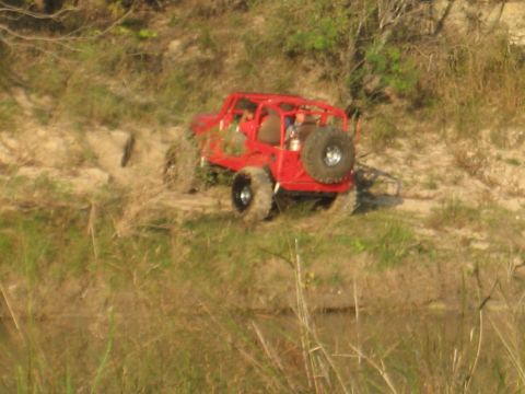 2001 Jeep Wrangler - A red off-road buggy with a roll cage navigates a dirt path beside a body of water.