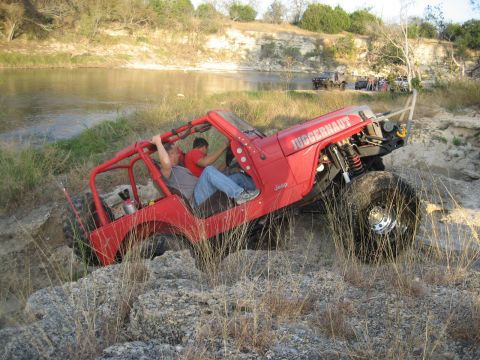 2001 Jeep Wrangler - Modified Jeep Wrangler navigates a rocky trail beside a river, with other vehicles visible in the background.