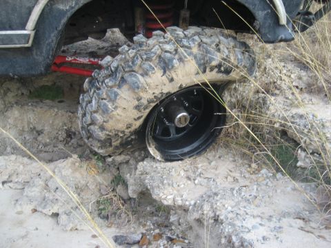 2001 Jeep Wrangler - A vehicle's tire is stuck in a dirt embankment, showing its aggressive tread and black rim.
