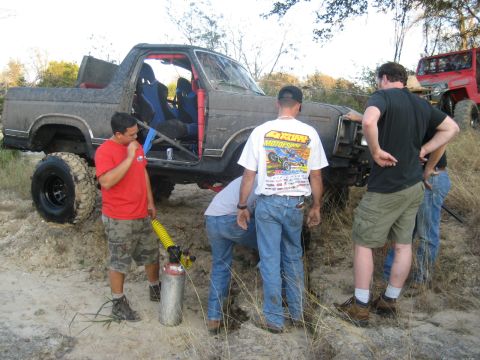 2001 Jeep Wrangler - A group of people attend to a heavily modified SUV, with another red off-road vehicle visible in the background.