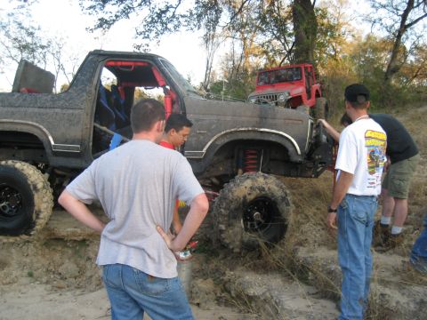 2001 Jeep Wrangler - Several people are gathered around two mud-covered off-road vehicles in a wooded area.