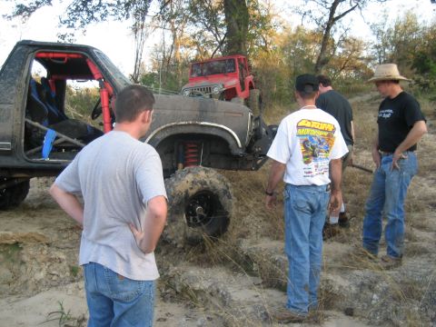2001 Jeep Wrangler - Several men observe two heavily modified off-road vehicles stuck in a muddy, wooded area.