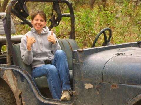 2001 Jeep Wrangler - A woman smiles and gives a double thumbs-up while sitting in the driver's seat of an older, open-top Jeep.
