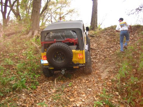 2001 Jeep Wrangler - A yellow Jeep Wrangler navigates an off-road trail, with a person walking up the hill beside it.
