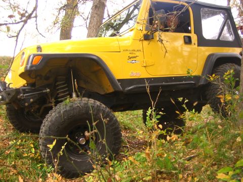 2001 Jeep Wrangler - A yellow 2001 Jeep Wrangler is shown from a 3/4 front angle on a wooded trail with autumn foliage.