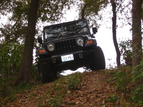 2001 Jeep Wrangler - A black 2001 Jeep Wrangler is seen from the front, navigating an off-road trail surrounded by trees.