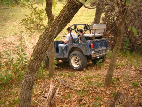 2001 Jeep Wrangler - A blue Jeep CJ-7 navigates a wooded trail with two occupants.