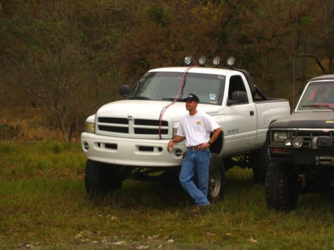 2001 Jeep Wrangler - A man poses with a lifted white Dodge pickup truck, parked next to another off-road vehicle.