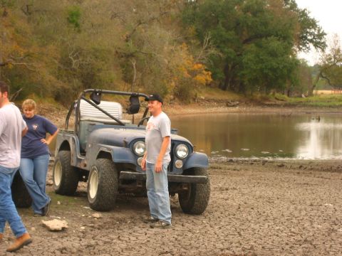 2001 Jeep Wrangler - A group of people stand around a vintage blue Jeep CJ near a body of water.