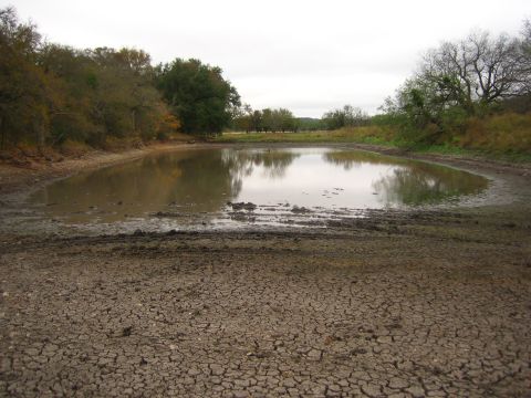 2001 Jeep Wrangler - A dry, cracked earth landscape surrounds a shallow, muddy pond with reflections of trees under a cloudy sky.