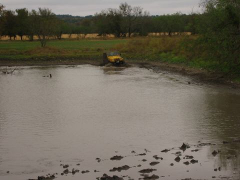 2001 Jeep Wrangler - A yellow 2001 Jeep Wrangler navigates through a muddy, water-filled area, kicking up spray as it goes.