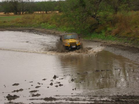 2001 Jeep Wrangler - A yellow Jeep Wrangler navigates through a shallow body of water, creating a splash.
