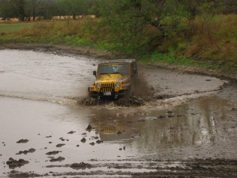 2001 Jeep Wrangler - A yellow 2001 Jeep Wrangler navigates a muddy off-road course, kicking up water and mud.
