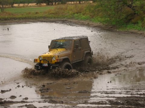 2001 Jeep Wrangler - A yellow 2001 Jeep Wrangler navigates a muddy terrain, kicking up spray as it drives through the mire.