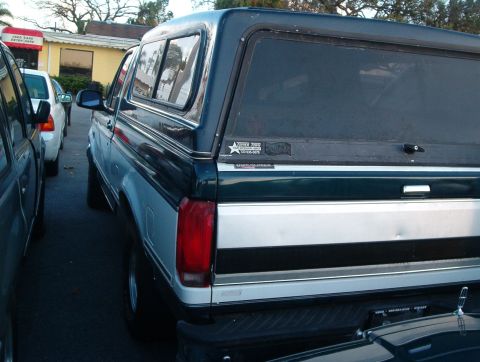 1995 Ford F-150 - A dark green and silver Ford Bronco with a camper shell is parked next to another vehicle.