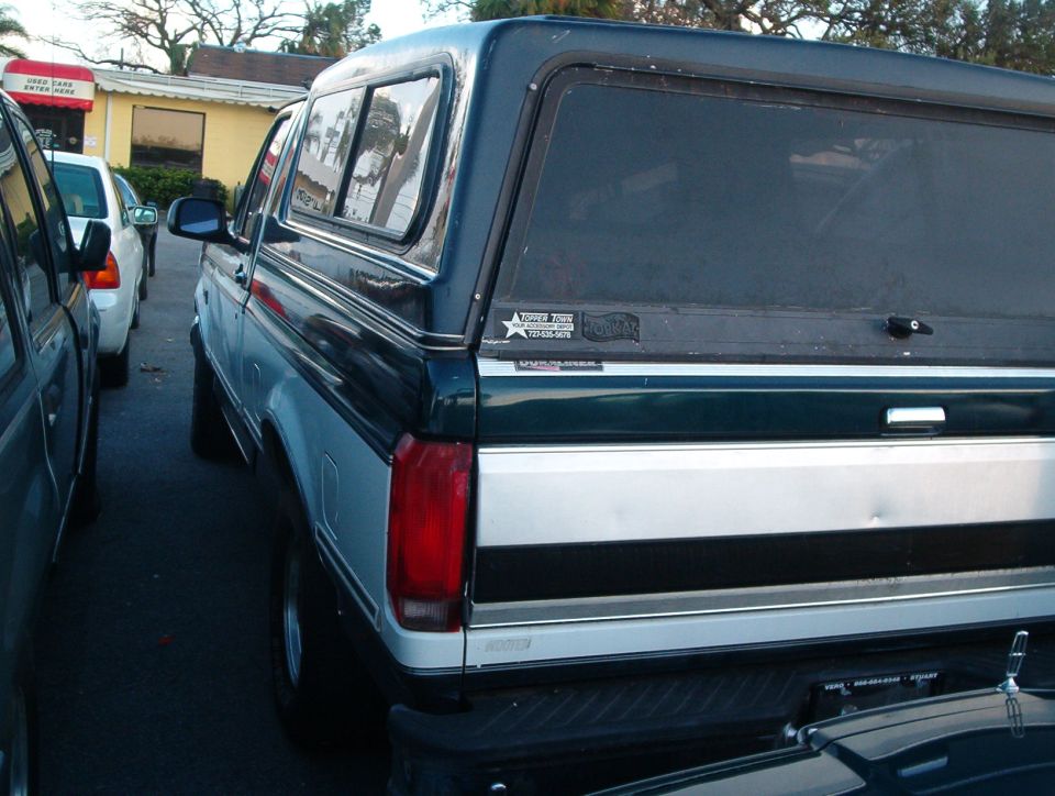 Dark green and silver Ford Bronco with a camper shell, seen from the rear
