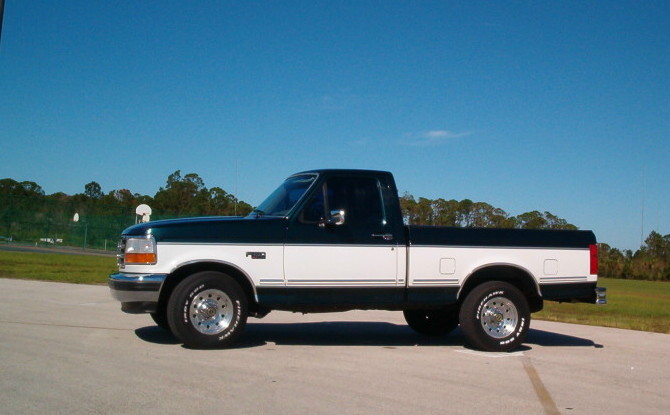Side view of a two-tone green and white 1995 Ford F-150 pickup truck parked on pavement