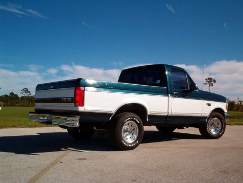1995 Ford F-150 - A two-tone green and white Ford F-150 truck is parked on pavement under a clear blue sky.