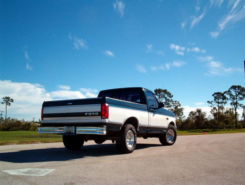 Rear view of a two-tone Ford F-Series truck parked on asphalt under a blue sky