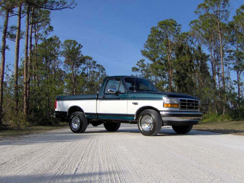 White and green 1995 Ford F-150 pickup truck parked on a dirt road