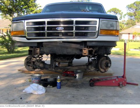 1995 Ford F-150 - The front suspension of a 1995 Ford F-150 is exposed and elevated for maintenance, with tools and parts nearby.