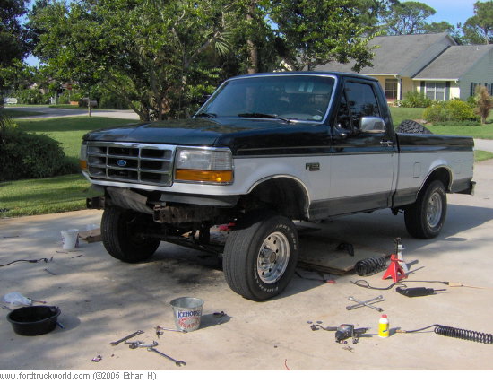 Two-tone black and silver Ford F-150 truck with a lifted suspension, parked on a driveway with tools scattered around