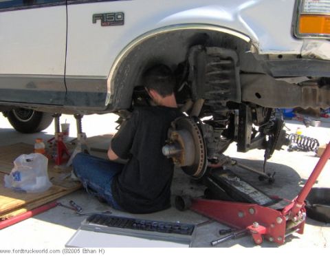 1995 Ford F-150 - Mechanic works on the front suspension of a 1995 Ford F-150, which is supported by jack stands.