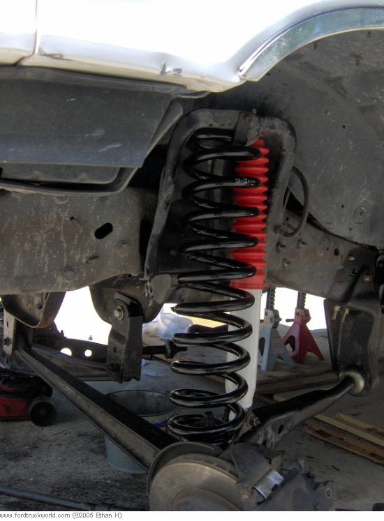 Close-up of a truck's front suspension with a new coil spring and red shock absorber boot