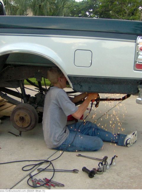 1995 Ford F-150 - Person grinding on the frame of a 1995 Ford F-150 during a modification.
