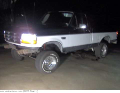 1995 Ford F-150 - A lifted pickup truck is shown at an angle with its headlights on at night.
