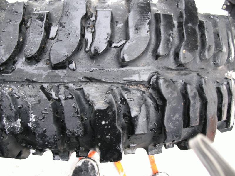 Close-up of a knobby off-road tire tread with water droplets. Part of a wheel rim is visible