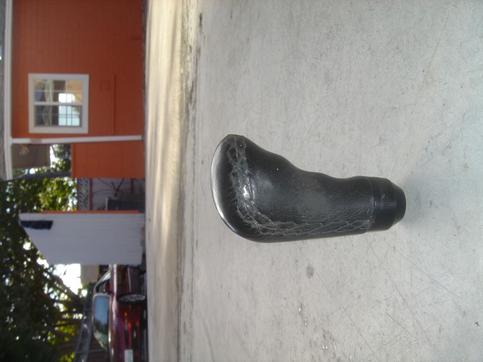 Black stitched leather shift knob sitting on concrete pavement outdoors