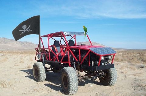 1993 Ford Bronco - A custom red off-road buggy flies a pirate flag and sports a parrot perched on its roof in a desert landscape.