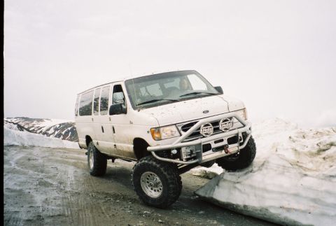 2000 Ford E350 - 3/4-front view of a white lifted Ford Econoline 4x4 van on a snowy gravel pass, fitted with a tubular front bumper, winch and a pair of rou…