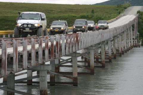 2000 Ford E350 - A convoy of off-road vehicles traverses a narrow bridge, heading towards a hill.