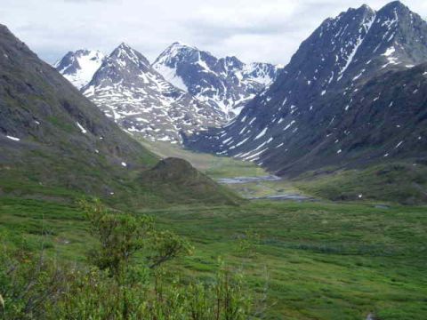 2000 Ford E350 - A vast mountain valley unfolds under a cloudy sky, with snow dusting the peaks and lush green grass covering the lower slopes.