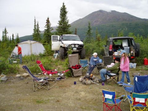 2000 Ford E350 - People enjoy camping with their vehicles in a wooded area with a mountain in the background.
