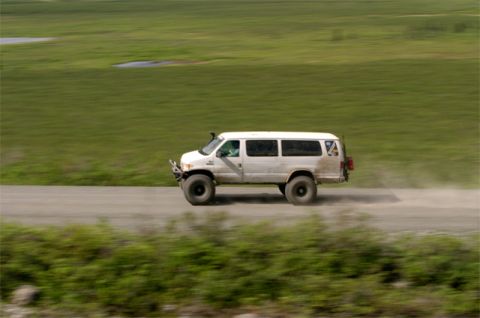 2000 Ford E350 - A white 2000 Ford E350 van, modified with off-road tires and a snorkel, kicks up dust as it drives along a dirt road.