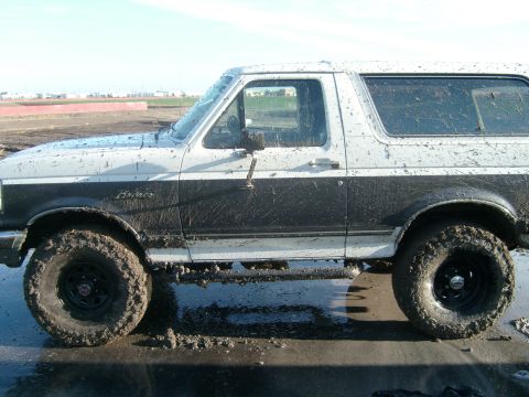 1989 Ford Bronco - A muddy Ford Bronco is shown from the side, its body covered in dirt and grime.
