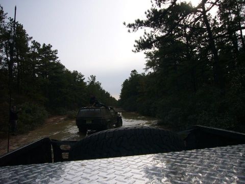 1989 Jeep Cherokee - Two vehicles navigate a muddy trail surrounded by dense forest under an overcast sky.