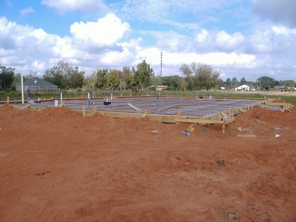 Construction site with concrete foundation and plumbing pipes under a cloudy sky