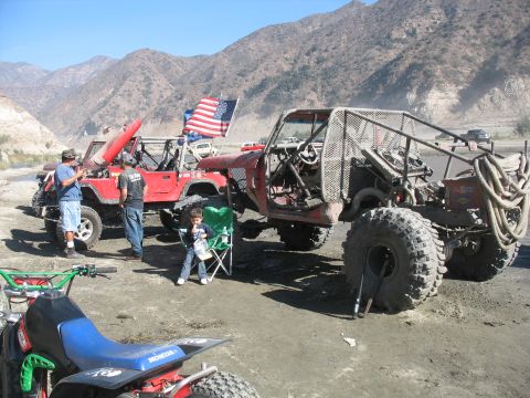 1987 Ford Bronco - Two heavily modified off-road vehicles are parked in a dry, mountainous landscape under a clear blue sky.