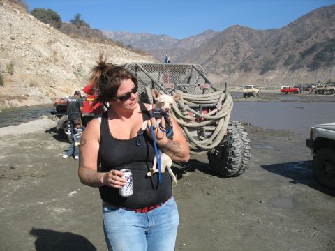 1987 Ford Bronco - A woman holds a small dog while standing near a custom off-road vehicle in a desert landscape.