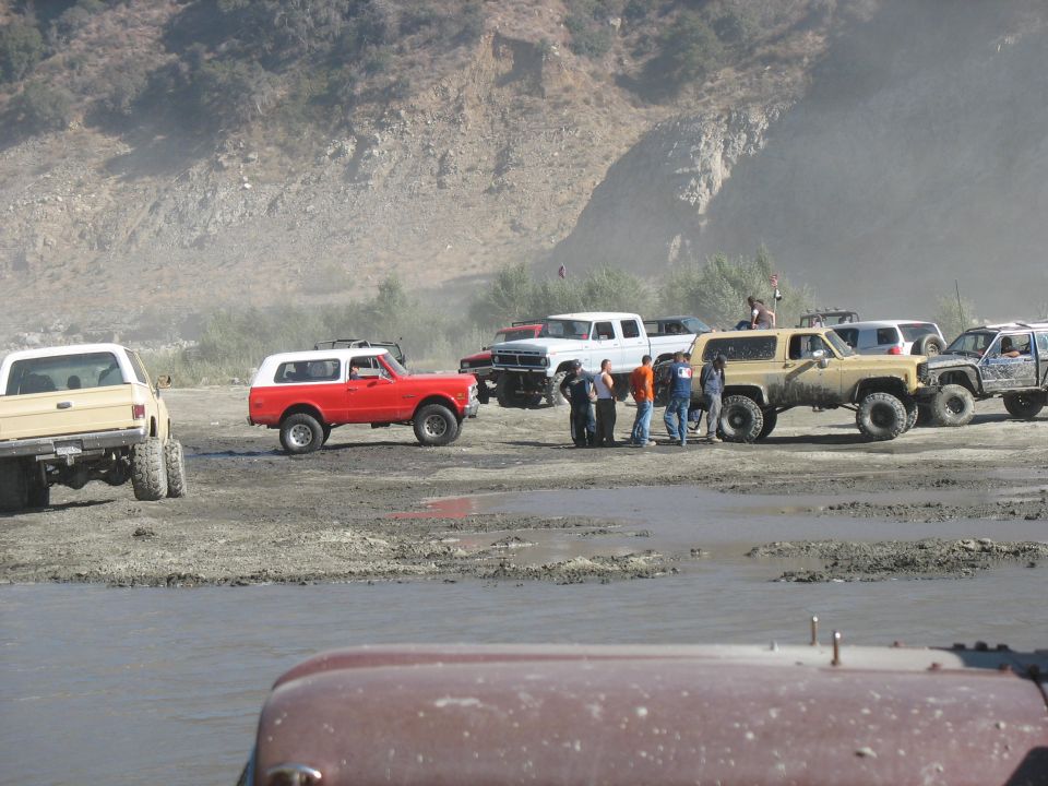 Several off-road vehicles, including a red Bronco and a tan Blazer, parked in a muddy, outdoor area
